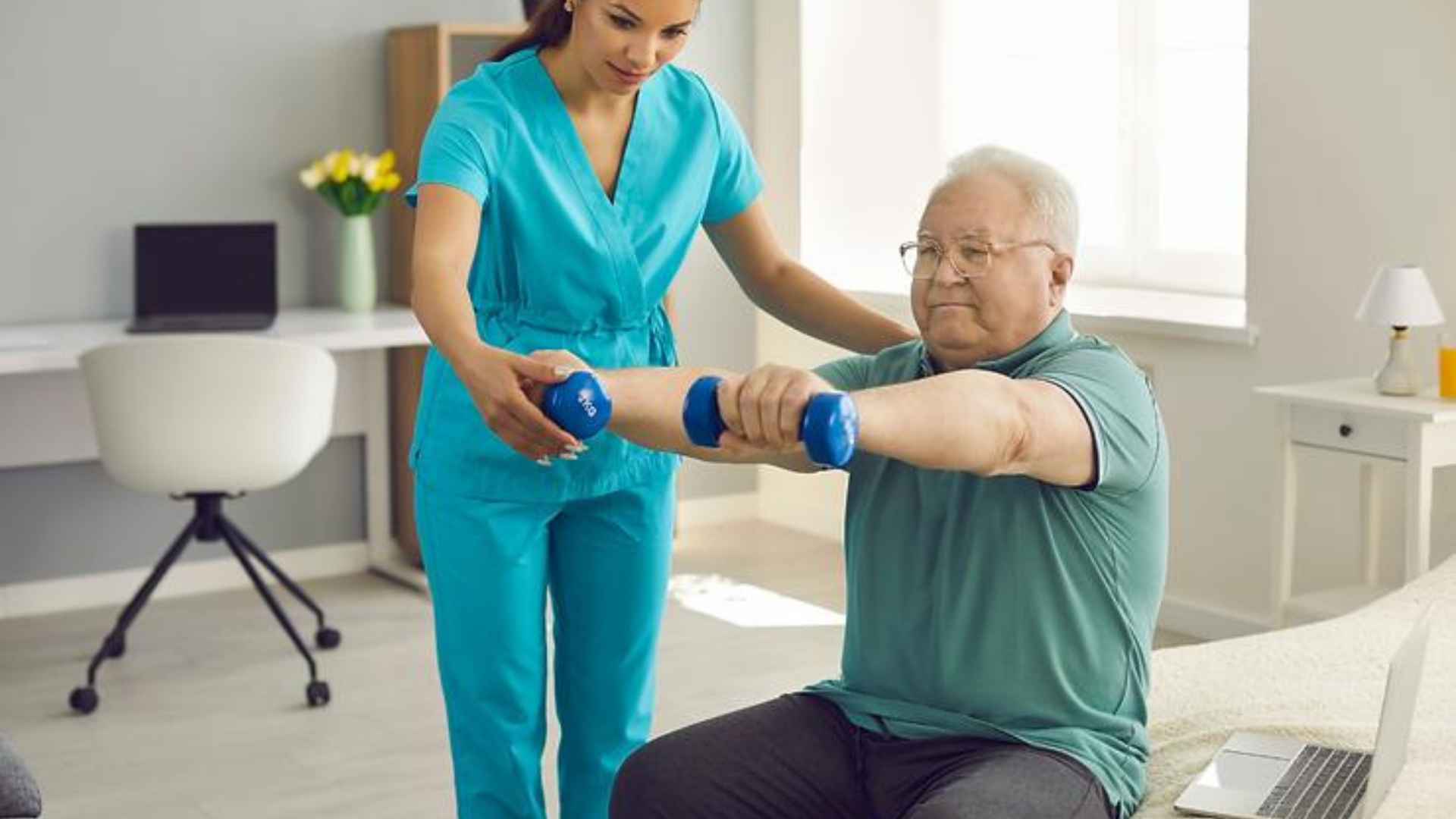An older man sat on a bed with weights in his hands doing an exercise with his physio