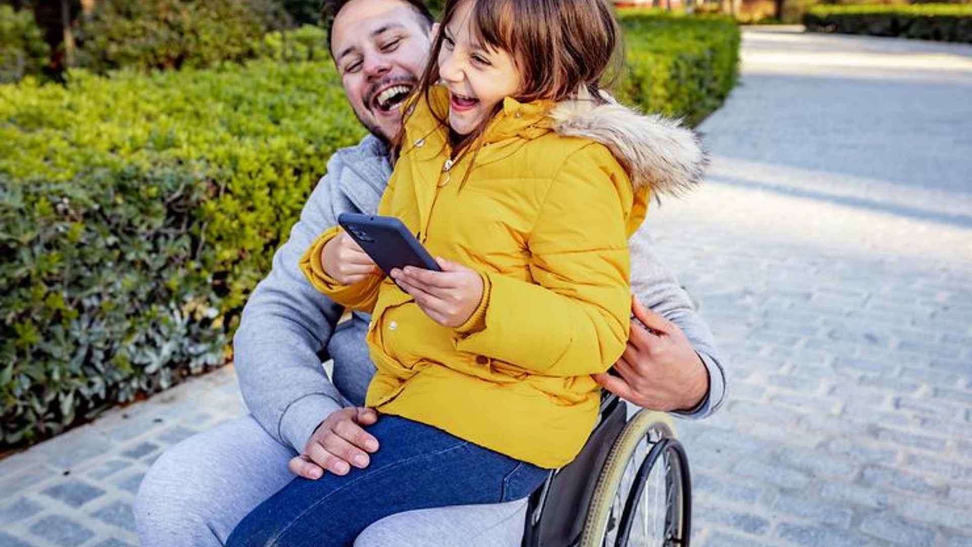 A man in a wheelchair with a young girl on his knee, both smiling