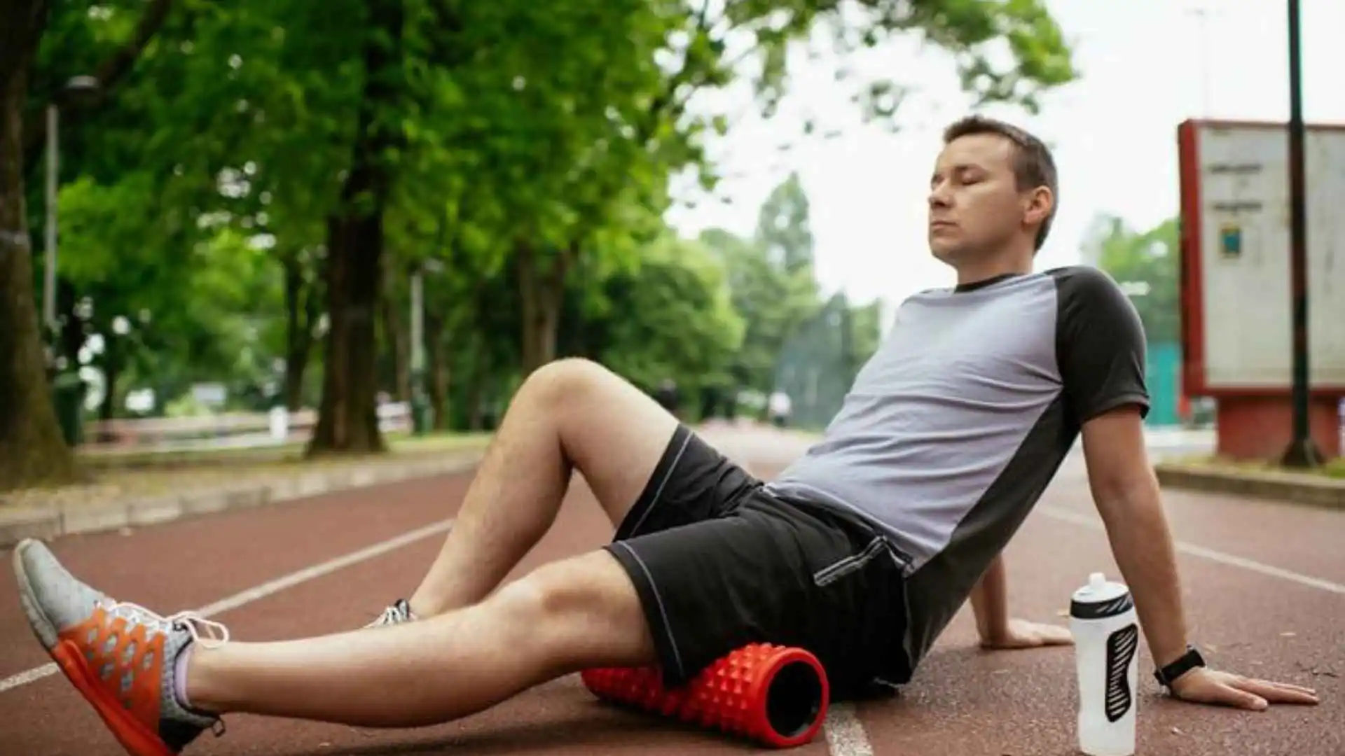 A man using a red foam roller on an athletics track